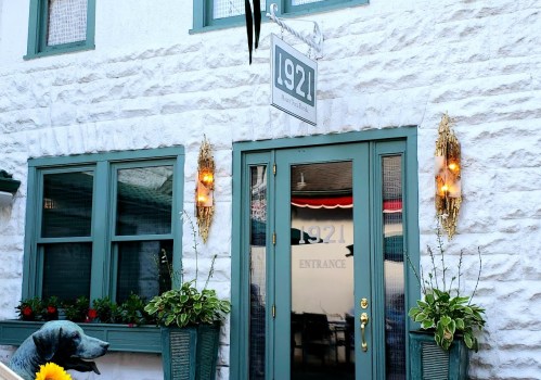 A charming entrance to a building with a sign reading "1921," surrounded by greenery and decorative lights.