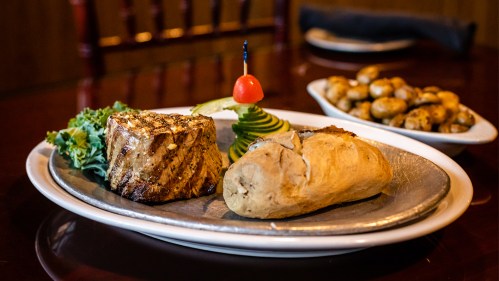 Grilled fish fillet with a decorative cherry, served with a baked potato and greens on a silver platter.