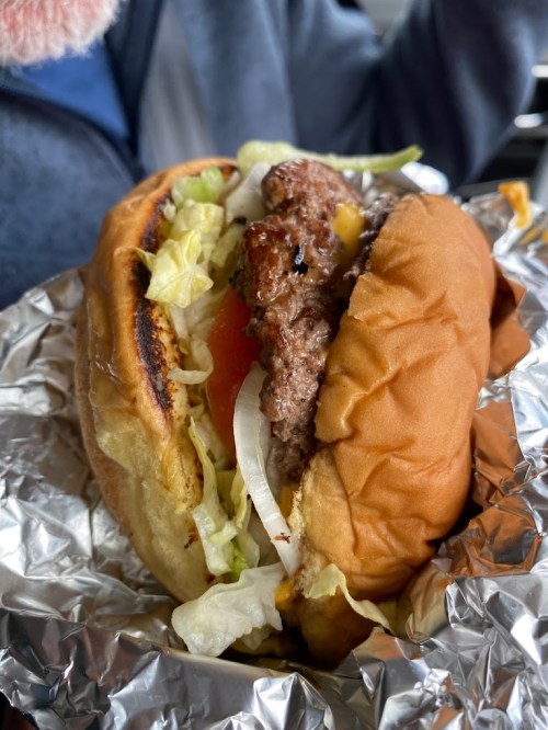 A close-up of a juicy hamburger with lettuce, tomato, and onion, wrapped in foil.