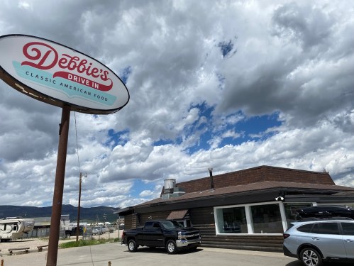 Sign for Debbie's Drive-In with a cloudy sky and classic American diner exterior. Cars parked outside.