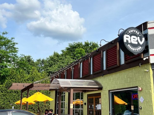 Exterior of Rev Coffee Roasters with yellow umbrellas, a sign, and a blue sky with clouds.