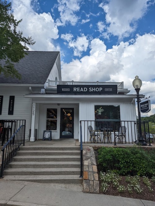A charming bookstore called "Read Shop" with a welcoming entrance and outdoor seating under a blue sky.