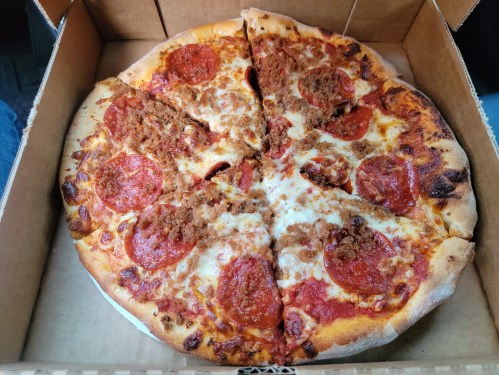 A pizza with pepperoni and sausage, partially sliced, in a cardboard box.