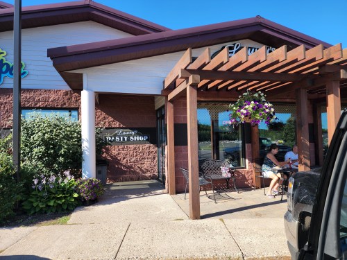 A pastry shop with outdoor seating, flowers hanging from a pergola, and customers enjoying their time outside.