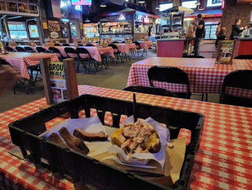 A table in a restaurant with checkered tablecloths, featuring a basket of barbecue meat and a partially eaten bun.
