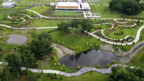 Aerial view of a landscaped park featuring winding paths, ponds, and greenery surrounding a modern building.