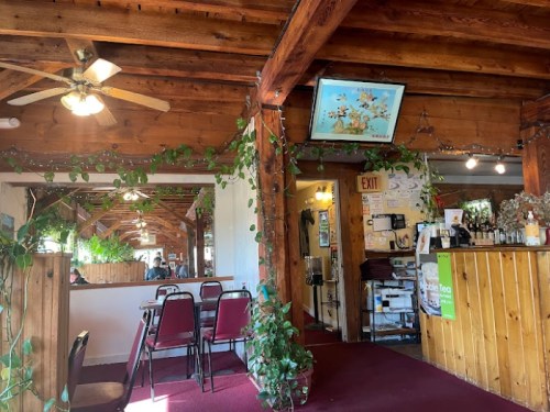 Cozy restaurant interior with wooden beams, plants, and a TV, featuring red chairs and a warm, inviting atmosphere.