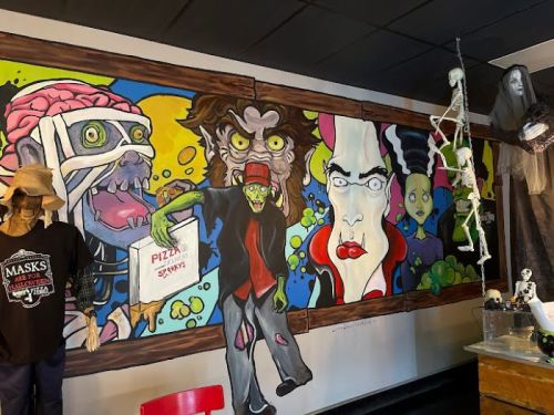 Colorful mural featuring a zombie, a monster, and abstract faces, with Halloween decorations in a themed setting.