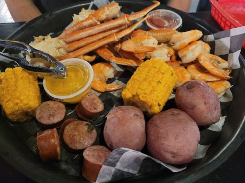 A platter of seafood featuring shrimp, crab, corn, potatoes, and sausage, served with dipping sauces.
