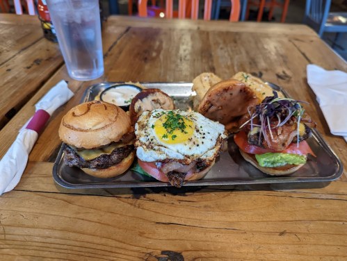 A metal tray with two gourmet burgers topped with lettuce, tomato, and a fried egg, served on a wooden table.