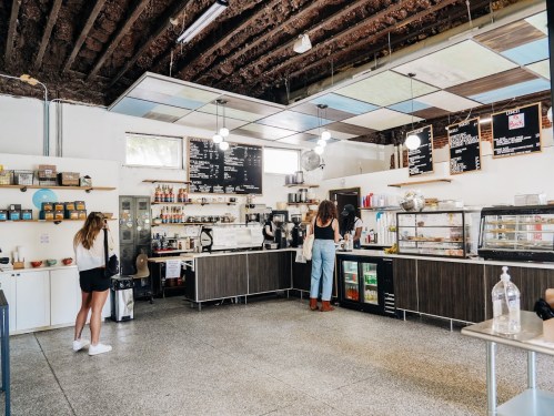 A modern café interior with a counter, menu boards, and two customers ordering drinks. Bright and spacious atmosphere.