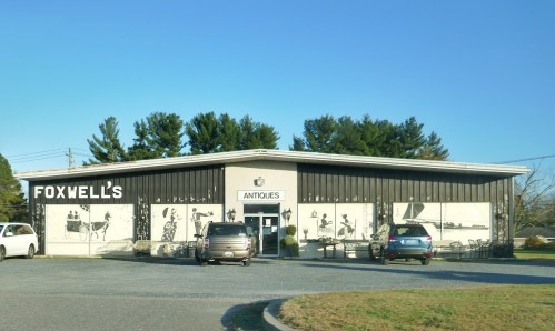 A building with "Foxwell's Antiques" sign, featuring large mural-style artwork on the facade and parked cars in front.
