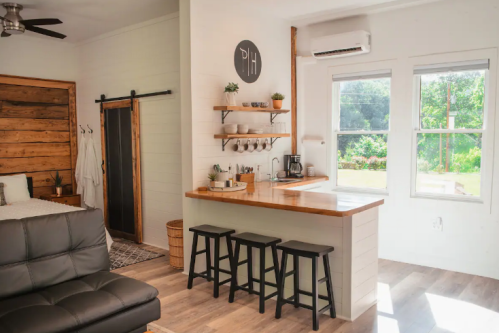 Cozy interior featuring a kitchen area with wooden shelves, a dining counter, and a bed in a bright, modern space.
