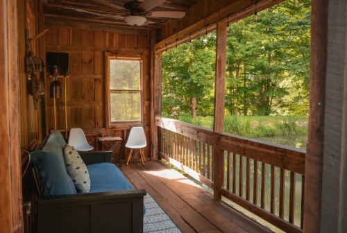 Cozy porch with wooden walls, two chairs, a small table, and a view of greenery outside.
