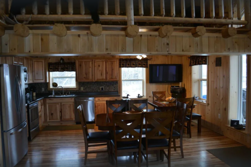 Cozy wooden cabin interior featuring a dining table, kitchen appliances, and large windows for natural light.