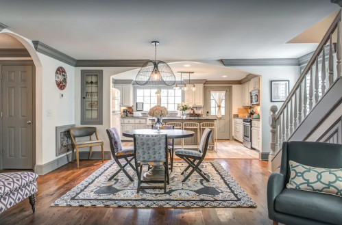 A modern kitchen and dining area with a round table, chairs, and stylish decor, featuring wood floors and gray accents.