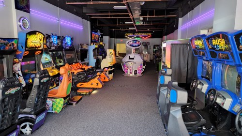 A vibrant arcade filled with various colorful gaming machines and seating, illuminated by neon lights.