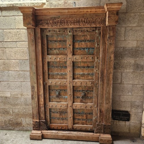 An ornate wooden door with intricate carvings and metal studs, set against a stone wall.