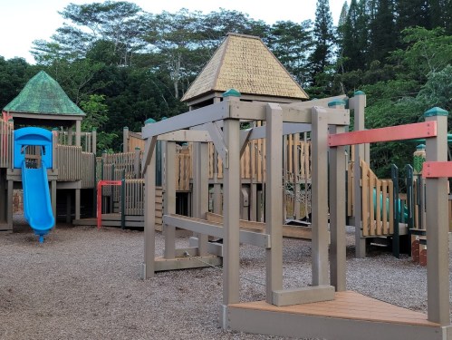 Colorful playground equipment with slides and climbing structures, surrounded by trees and greenery.