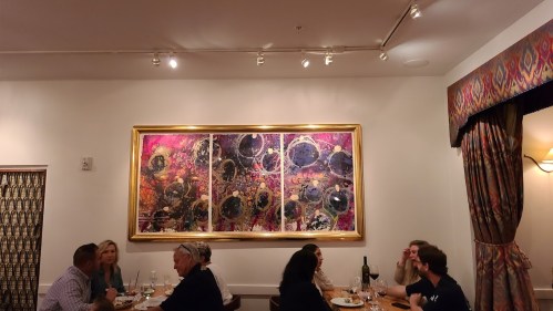 A restaurant interior featuring diners and a large, colorful abstract artwork on the wall.