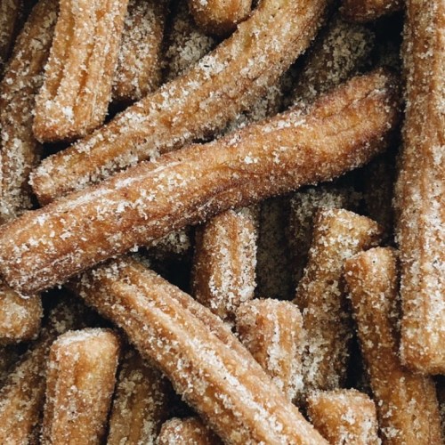 A close-up of golden-brown churros coated in sugar, piled together in a tempting arrangement.