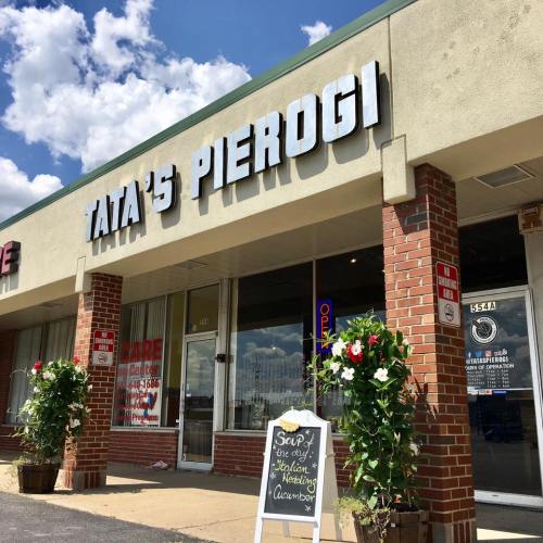 Exterior of Tata's Pierogi restaurant with a sign, flower arrangements, and a chalkboard menu outside.
