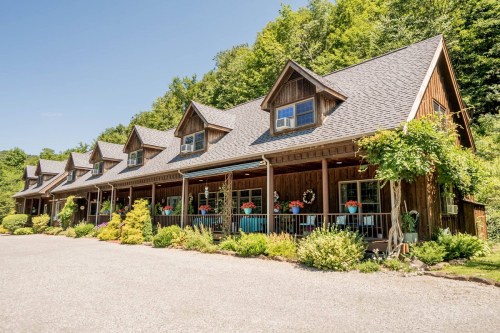 A charming wooden lodge with multiple gabled roofs, surrounded by greenery and colorful flower pots on the porch.