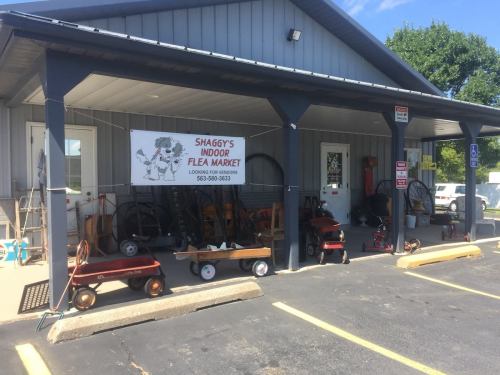 A storefront with a sign for "Shaggy's Indoor Flea Market," featuring various items and wagons outside.