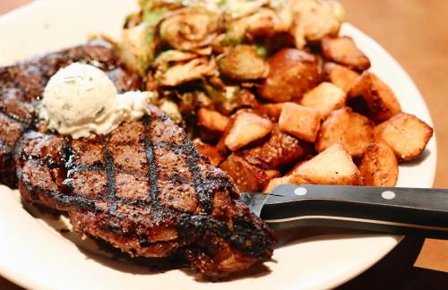 A grilled steak topped with butter, served with roasted potatoes and Brussels sprouts on a white plate.