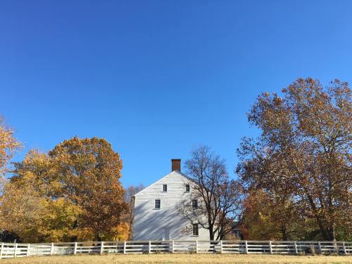 A white house surrounded by autumn trees under a clear blue sky, with a white fence in the foreground.