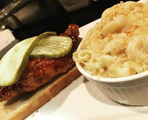 A plate featuring a fried chicken sandwich with pickles on bread, alongside a bowl of macaroni and cheese.