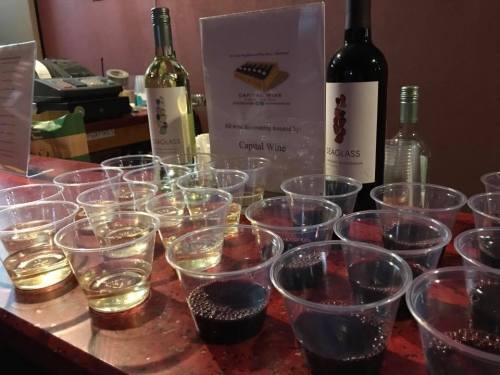 A table with various cups of white and red wine, alongside a sign about a wine tasting event.
