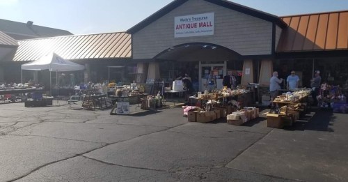 A bustling antique mall with outdoor vendors displaying various items for sale on a sunny day.