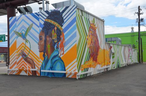 Colorful mural featuring a woman with a bird and a lion, set against vibrant geometric patterns on a building.