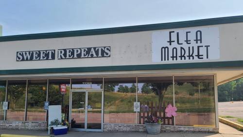 Exterior of a storefront featuring signs for "Sweet Repeats" and "Flea Market" under a clear blue sky.