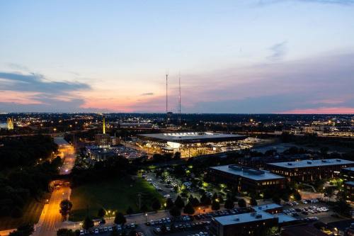 Aerial view of a city at dusk, featuring buildings, roads, and a stadium under a colorful sky.