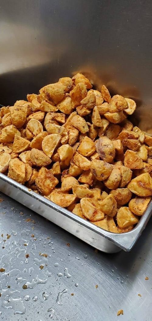 A metal tray filled with golden-brown, crispy fried potato wedges.