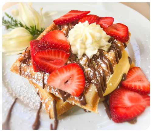 A delicious dessert featuring a waffle topped with strawberries, whipped cream, and chocolate drizzle on a white plate.
