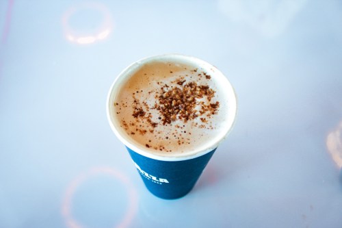 A coffee cup topped with a sprinkle of cinnamon sits on a light surface.