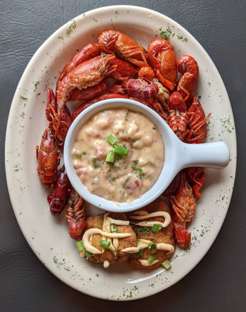 A plate of crawfish surrounding a bowl of creamy seafood stew, garnished with green onions and herbs.