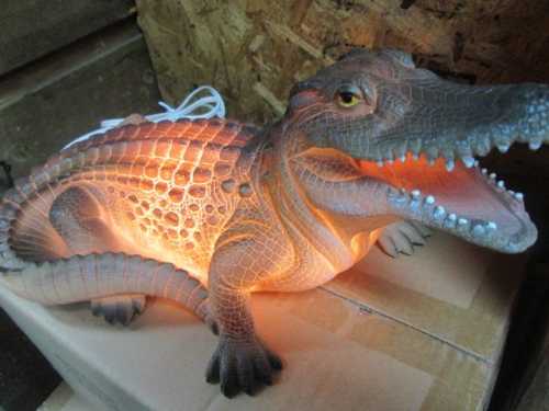 A crocodile-shaped lamp with a glowing interior, resting on a cardboard box.