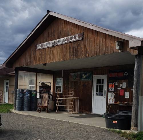 A rustic wooden building with a sign reading "The Pioneer Place, U.S.A." and a porch, under a cloudy sky.