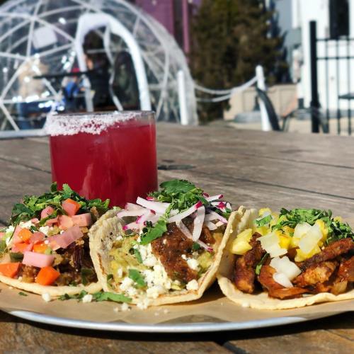 A plate of colorful tacos topped with various ingredients, alongside a refreshing drink on a wooden table.