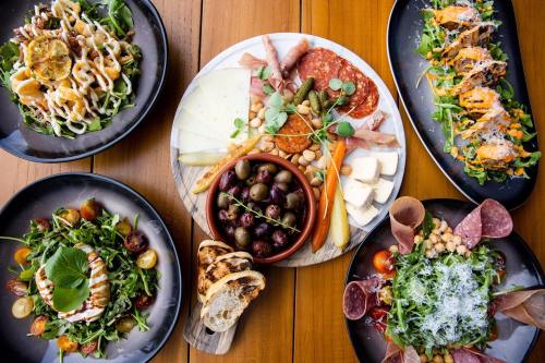 A variety of gourmet salads and charcuterie, featuring greens, meats, cheeses, olives, and colorful garnishes on wooden table.