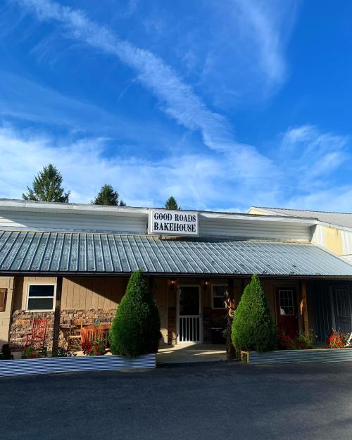 Exterior of Good Roads Bakehouse, featuring a metal roof, sign, and landscaped entrance under a blue sky.
