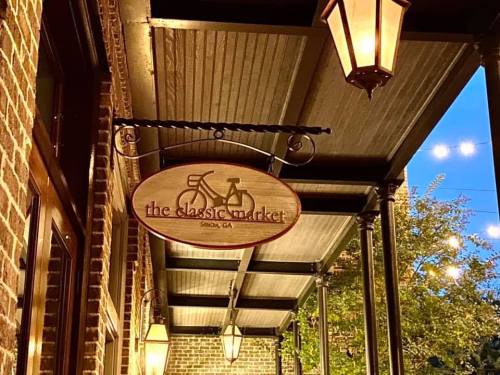 Sign for "the classic market" featuring a bicycle design, hanging under warm lanterns in a charming outdoor setting.