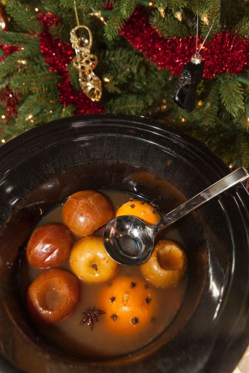 A black bowl filled with spiced apples and oranges, surrounded by festive holiday decorations.