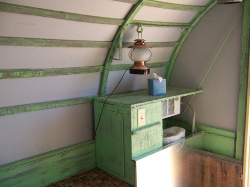 Interior of a small, rustic space with green wooden beams, a lantern, and a small air conditioner on a wooden counter.