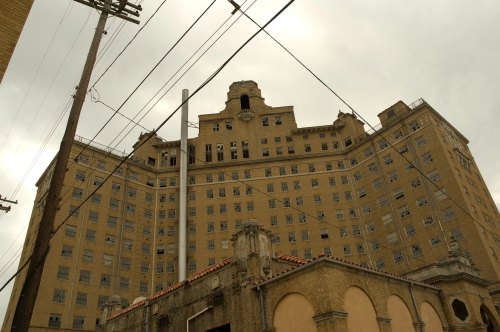 Abandoned multi-story building with broken windows, under a cloudy sky, surrounded by power lines.