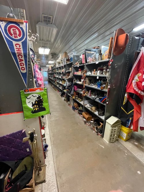A narrow aisle in a thrift store lined with shelves of various items, including bags, clothing, and decorations.
